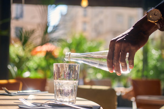 Man is holding bottle with still water and pouring it to the glass.