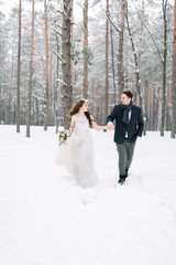 Fototapeta na wymiar Winter wedding in a snowy forest, lovely couple holding hands, looking each other, walking outdoors in winter forest