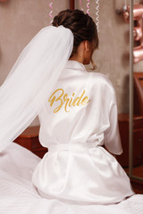 close up portrait  a  stylish  bride in a robe with long veil  with the inscription "the bride". brides morning in the hotel room. wedding morning.