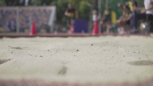 Sportsman doing long jump landing in the sandpit. Track and field championships. An athlete competing in the long jump.