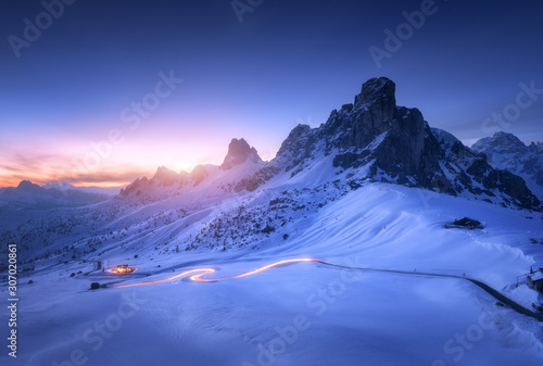 Snowy Mountains And Blurred Car Headlights On The Winding Road At Night In Winter Beautiful Landscape With Snow Covered Rocks House Mountain Roadway Blue Starry Sky At Sunset In Dolomites Italy Wall Snowy Mountains And Blurred Car Headlights On The Winding Road At Night In Winter Beautiful Landscape With Snow Covered Rocks House Mountain Roadway Blue Starry Sky At Sunset In Dolomites Italy Wall