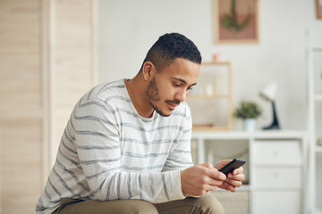 Side view portrait of modern mixed-race man using smartphone in home in home interior, copy space