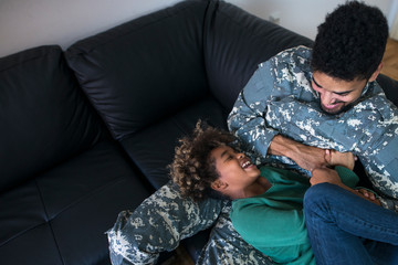 Soldier in uniform spending time with his family while off service. Father and daughter playing on couch.