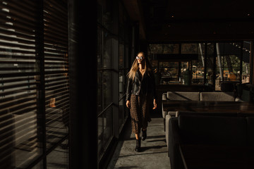 beautiful girl model in a restaurant in a beautiful loft interior. on the eyes of sunglasses, dressed in a leather black jacket, casual clothes. warm photography, sunlight
