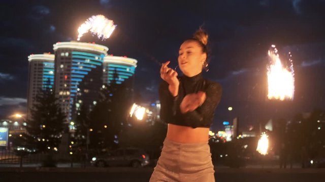Performance or show with fire outdoor. Adult girl moves with flaming torches with group of fireshow artists. Concept of modern arts and culture. Slow motion, city landscape.