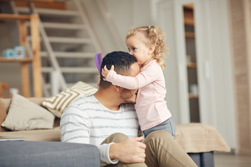 Portrait of cute little girl kissing father on head while enjoying time together at home, copy space