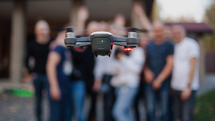 Flying drone, against the background of the company of young people. Unmanned aerial vehicles. Photos and videos from the drone.