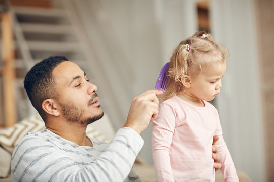 Portrait Of Caring Stay At Home Dad Brushing Hair Of Cute Little Daughter At Home