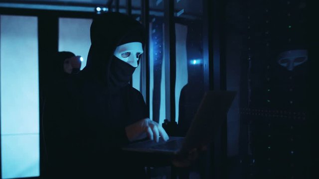 Masked network hacker using laptop to break a server in digital room. Scared computer spy making electricity error data center blackout running away. Unrealized cybercrime.