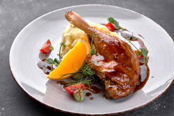 Cooked duck leg in sauce, with mashed potatoes, on a dark background
