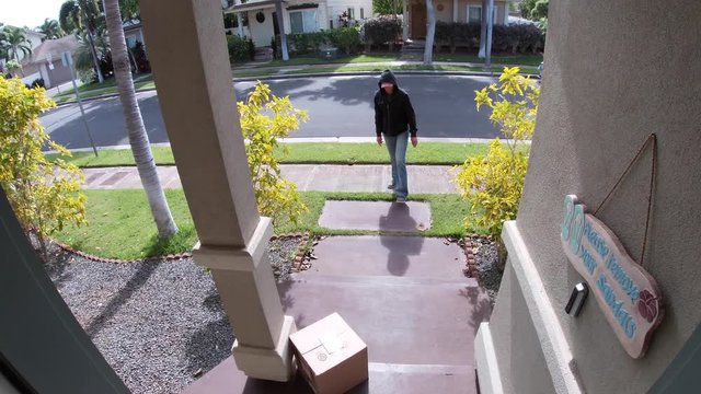 Person stealing delivery package from porch steps, surveillance camera view