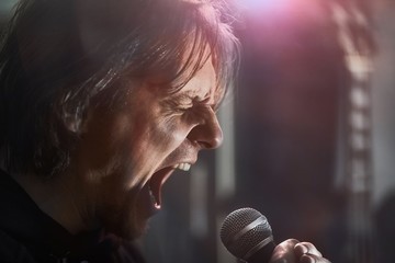 Metal singer yelling into the microphone with mouth wide open and eyes closed