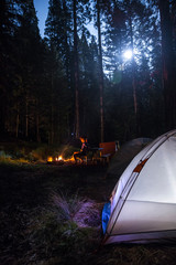 Night time photograph of someone camping and sitting by the fire in the forest.  Taken in Mineral King, California.  