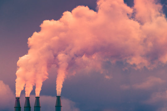 Smoke and steam rising into the air from power plant stacks; dark clouds background; concept for environmental pollution and climate change