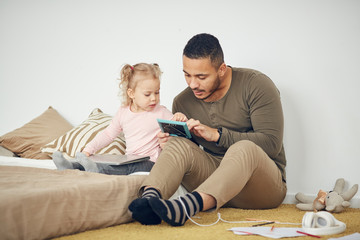 Full length portrait of cute litte girl looking at framed family photos with dad, copy space