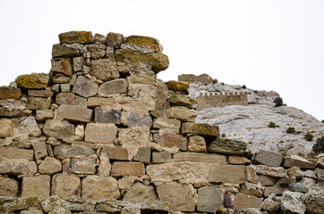 Tower and wall of an old fortress in the mountains. Ruins and excavations.