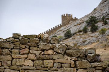 Tower and wall of an old fortress in the mountains. Ruins and excavations.