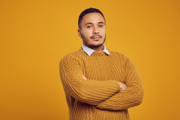 Waist up portrait of young African-American man wearing knit sweater posing confidently against yelow background in studio, copy space