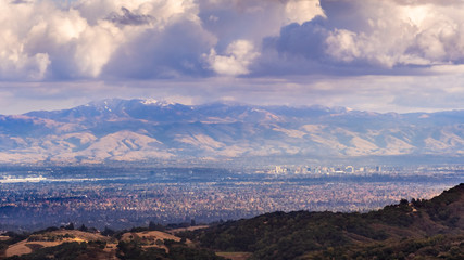 Fototapeta na wymiar Aerial view San Jose, part of Silicon Valley; snow is visible on top of Mount Hamilton (part of Mount Diablo mountain range); storm clouds cover the sky; San Francisco Bay Area, California