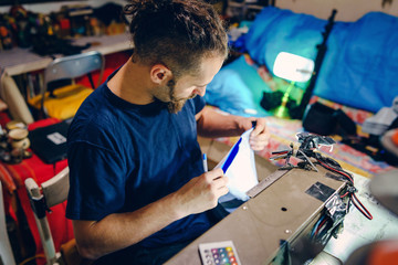 High angle view on young adult male man tailor working by his sewing machine at workshop making a bag checking stitches quality handmade creative