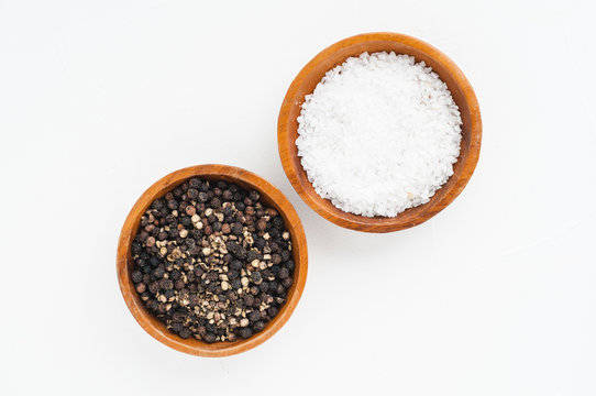 wooden bowls of salt and pepper on a white textured background