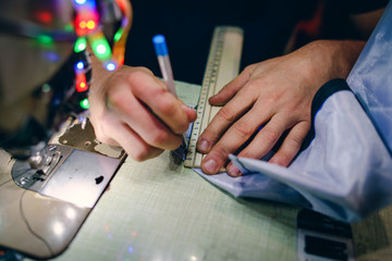 close up on hands pen tailor using ruler to measure and mark the fabric material by the sawing machine on the table at work shop workshop craft