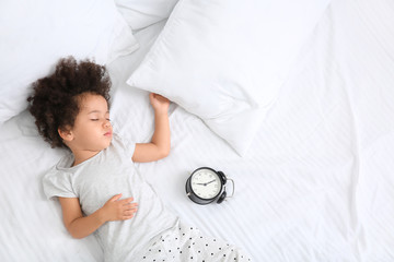 Little African-American girl with alarm clock sleeping in bed