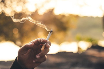 Men hand caught a burning cigarette causing smoke, concept stop smoking.