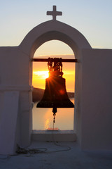 An intense sunset in Oia hidden behind a church bell, located in the stunning island of Santorini, Greece