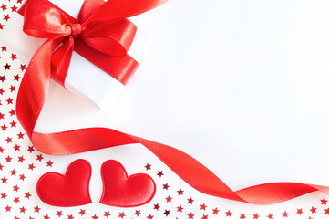 Gift or present box with red ribbon, decorative hearts and stars confetti on white background. Holiday concept, flat lay, top view.