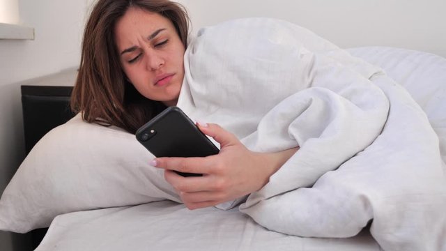 Sleepy brunette woman waking up in bed in the morning and does not want to get out of bed. not a good morning. 4k