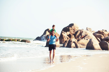 happy family on beach playing, father with son walking sea coast, rocks behind smiling taking vacation