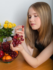 Girl, teenager, at the table eats grapes