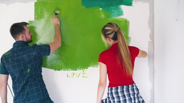 lovely young man in blue shirt and smiling woman in red paint white wall with word love in repairing room backside view