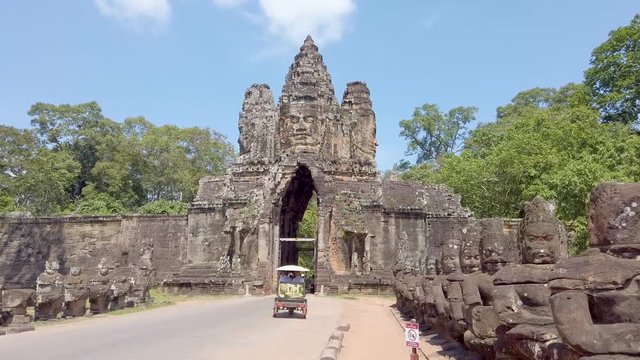 Tourists driving scooters and tuk tuk through Angkor Thom gate entrance, Cambodia