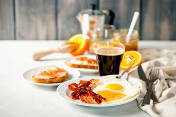 The English breakfast - eggs,  bacon,  toasts with ricotta and jam, juice in a glass, coffee on a grey background. Selective focus.