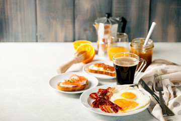 The English breakfast - eggs,  bacon,  toasts with ricotta and jam, juice in a glass, coffee on a grey background. Selective focus.