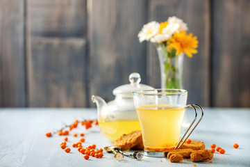 Vitaminic healthy sea buckthorn tea in small glass tea pot with fresh raw sea buckthorn berries. Sea-buckthorn tea and cookies.  Selective focus