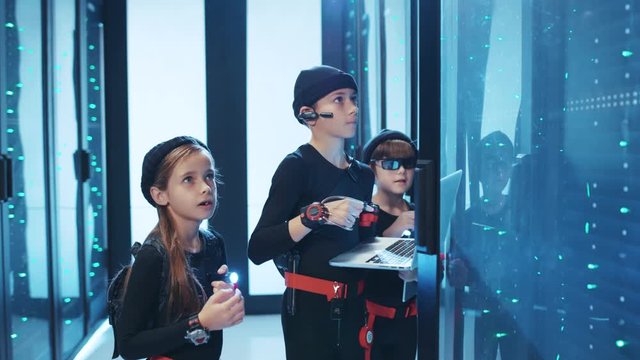Young hackers kids activating dark database server cabinet. Team of girl and boys secret agents inspecting server racks to steal important information. Cybercrime.