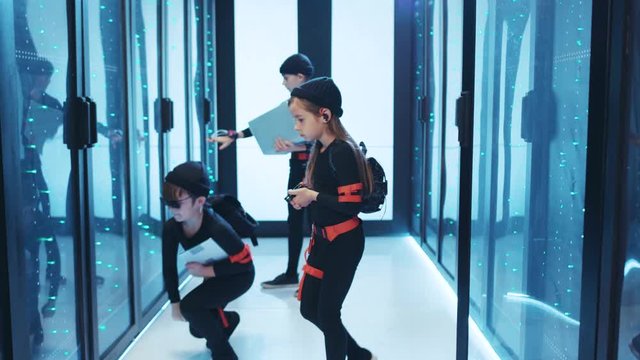 Team of professional kids agents sneaking into secure server room, inspecting rack cabinets with spy gadgets, cooperating on special mission at data center.