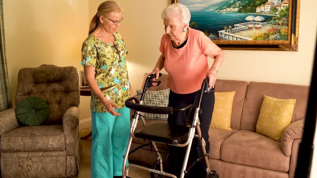 Closeup Of Home Healthcare Nurse Helps Elderly Woman Get Up From Couch And Use A Walker.