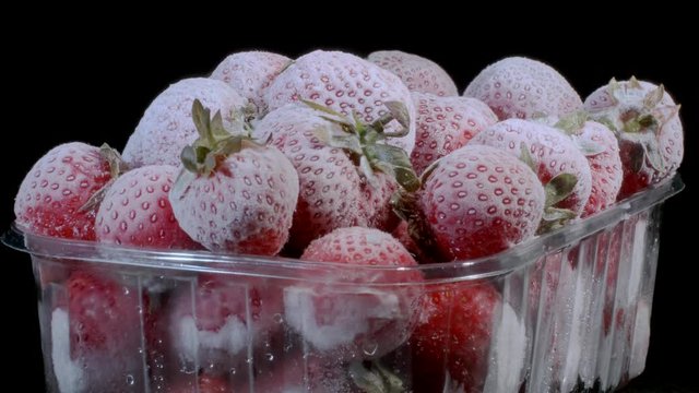Fresh frozen strawberries in disposable plastic food pack on black background. Rotation 360 degrees, closeup