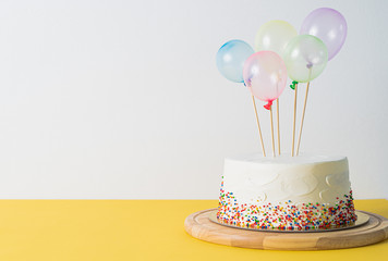 White Birthday cake and colorful balloons over light grey.food concept anniversary background.