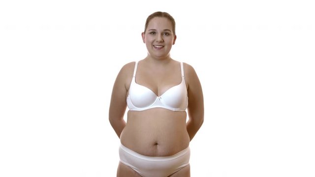 Smiling overweight woman in white underwear on white studio background.
