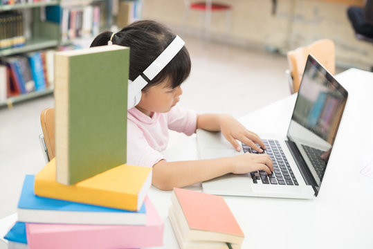 Girls are using computers to study library knowledge. She has earphones at her ear.