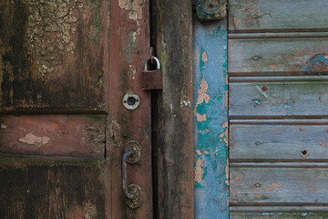 Fragment of an old closed wooden door with cracked brown paint. There is a metal handle and a rusty padlock. Background.