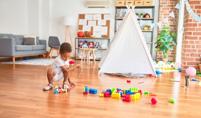 Beautiful african american toddler playing with wooden blocks train toy around lots of toys at kindergarten