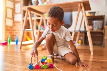 Beautiful african american toddler playing with wooden blocks train toy around lots of toys at...