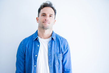 Young handsome man wearing denim shirt standing over isolated white background with serious expression on face. Simple and natural looking at the camera.