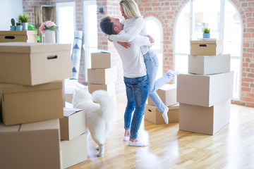Fototapeta na wymiar Young beautiful couple with dog hugging at new home around cardboard boxes